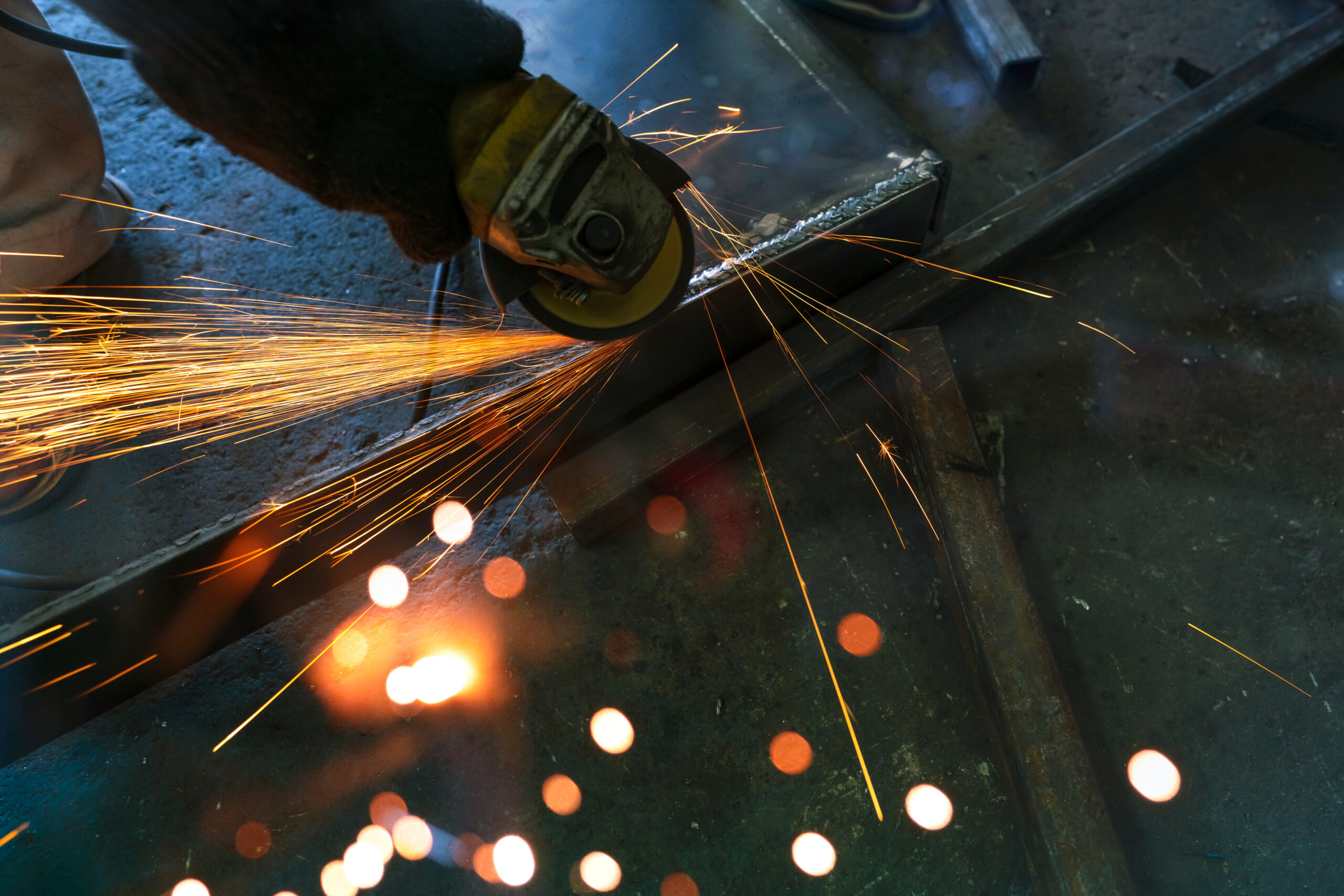 Industrial worker using angle grinder grinding metal on welding seams. Worker working with angle grinder and has sparks. Tool for cut steel. Safety in industrial workplace. Metal factory industry.